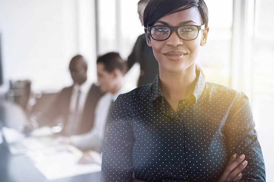 Smiling female professional with obscured male professionals at their desks in background