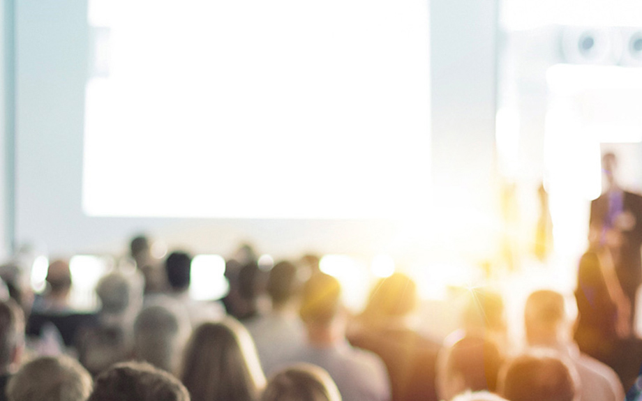 A blurry image of a symposium with a male speaker